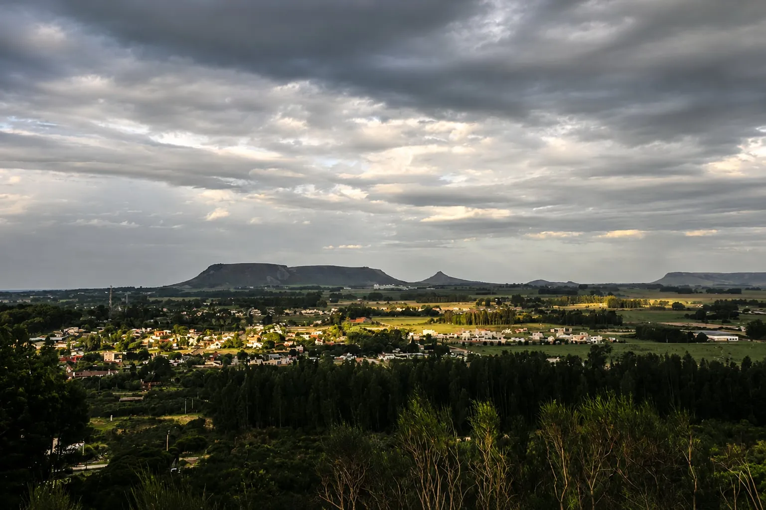 Vista del pueblo desde lo alto, con la sierra de cumbre plana en el horizonte y el cielo nublado