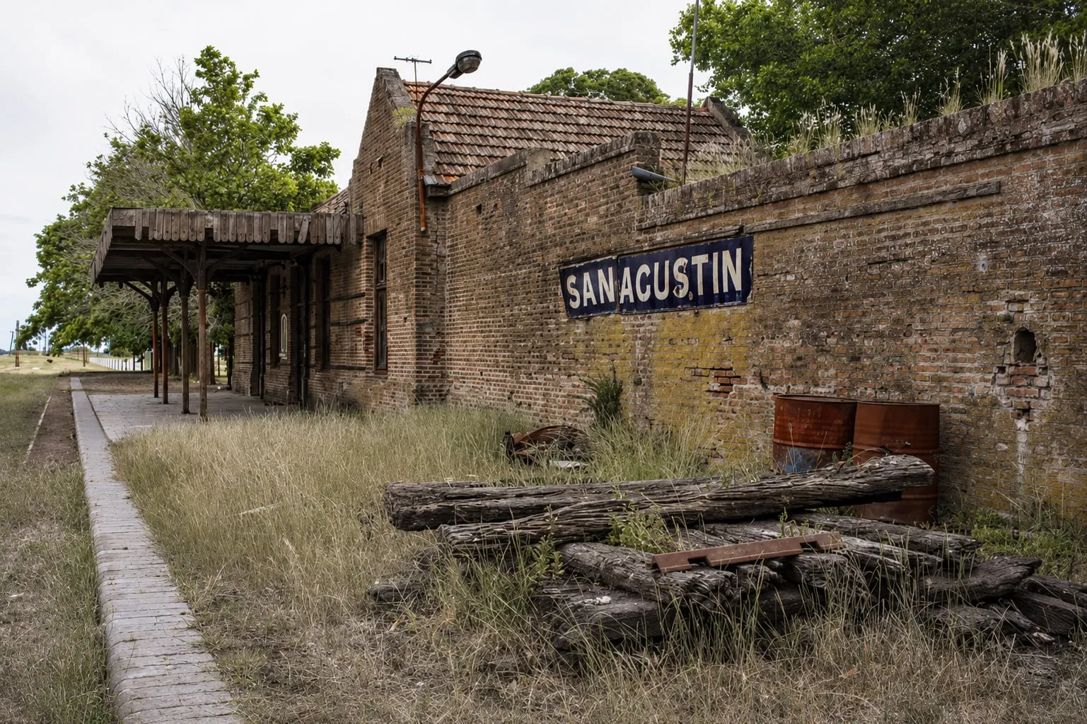 La vieja estación de tren de ladrillo, con el cartel esmaltado del andén y durmientes apilados contra la pared